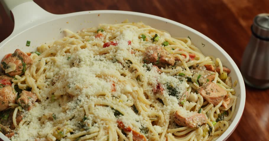 Delicious spaghetti with tender salmon pieces, cherry tomatoes, and spinach in a creamy sauce. Italian seafood pasta cooking in a frying pan. 4K.