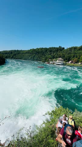 Rhine Falls viewed from the rocky lookout reveals Europe’s largest waterfall in its full dramatic power, as vast torrents of turquoise water surge over jagged cliffs below. Mist rises from the roaring cascade, catching the light and softening the surrounding landscape of forested hills and historic stone structures. From the rock viewpoint, the sense of scale is immersive and awe-inspiring, highlighting the raw energy of the Rhine River as it crashes through the heart of Switzerland’s natural scenery.