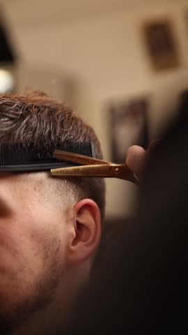 The barber is working. He is cutting hair in the barber shop.