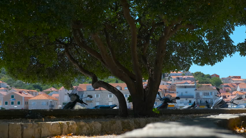 Scenic mediterranean old town with scooters parked in the shade. Stunning view of a picturesque mediterranean town with terracotta roofs, viewed from a shaded promenade with several motorbikes parked