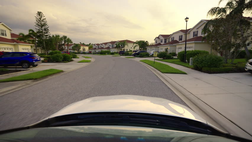 Car point of view. Vehicle driving on suburban street between condominium residential buildings in Florida residential area. Transportation and traffic concept.