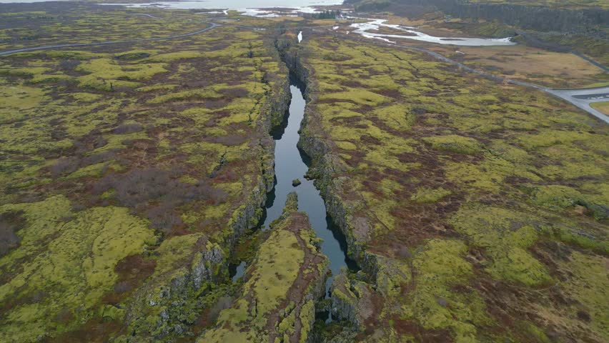 Aerial drone view of an Icelandic gorge at sunset, featuring green vegetation, warm evening light, and untouched Nordic wilderness.