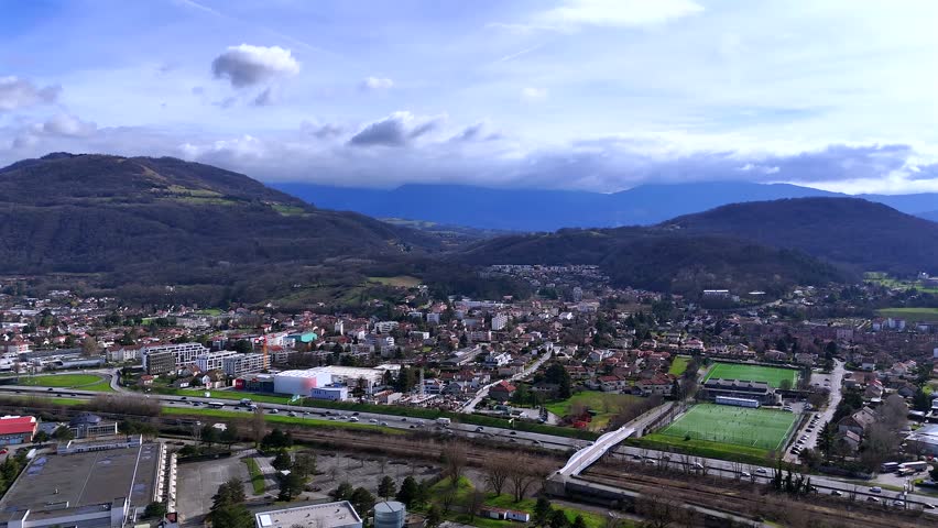 Drone view of Grenoble suburb with sports fields and dramatic cloudy hills
