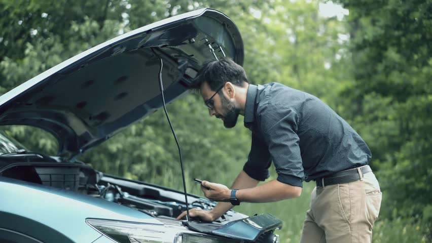Driver Trying To Fix Engine Problems Or Checking Oil Level During Road Trip Emergency. Driver Inspecting Open Hood Of Broken Car. Troubleshooting Vehicle Failure. Automotive Accident Technical Support