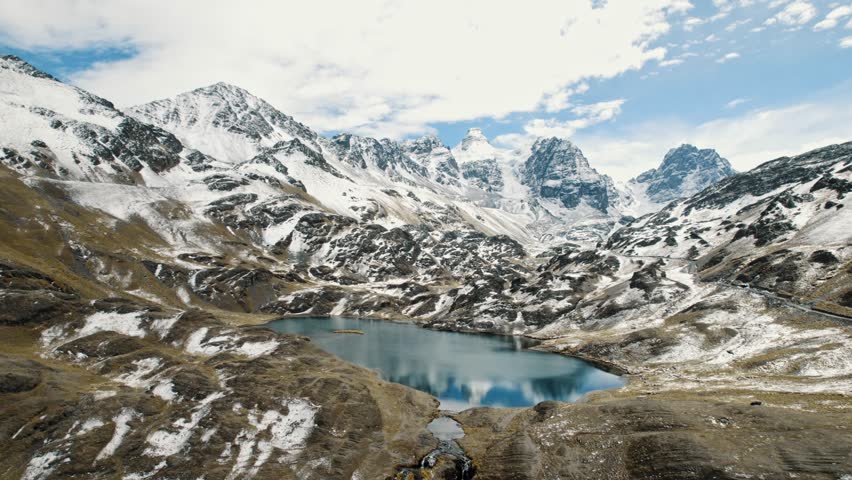 A cinematic dolly shot gliding over a blue alpine lake toward the snow-capped summits of Pico Austria. The rugged beauty of the Condoriri massif in the Bolivian Andes.
