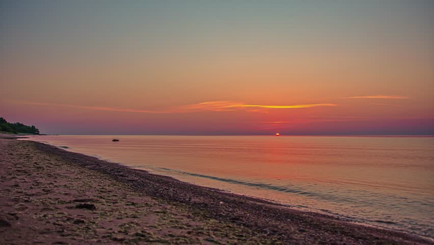 Time lapse sunrise over calm ocean water with sandy beach foreground