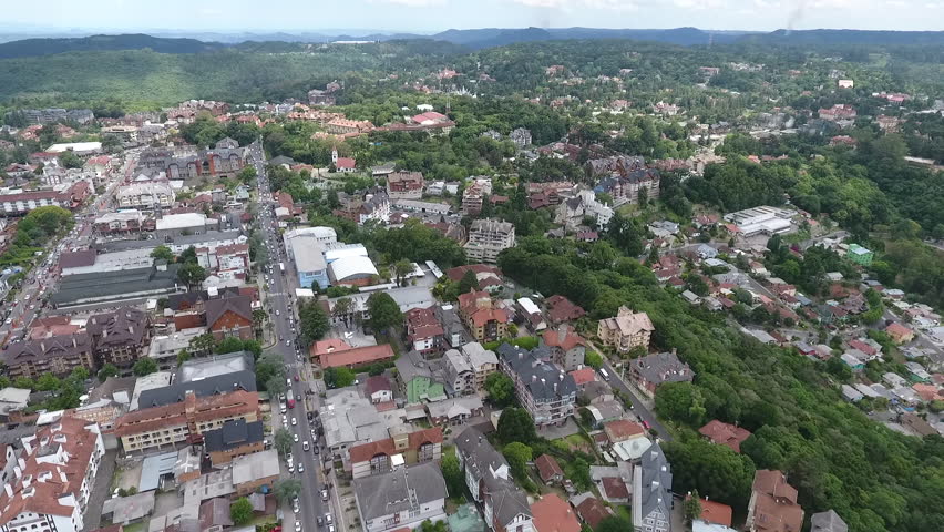 Cinematic drone aerial wide angle high altitude establishing shot of Gramado city center surrounded by urban hills and greenery in Rio Grande do Sul Brazil. High quality 1080p 60fps video.