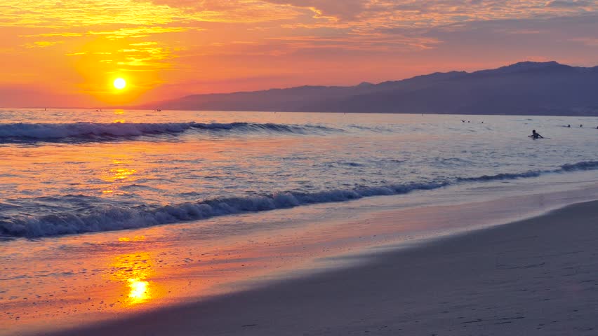 Stunning sunset over Pacific Ocean with rolling waves and mountain silhouette on California beach