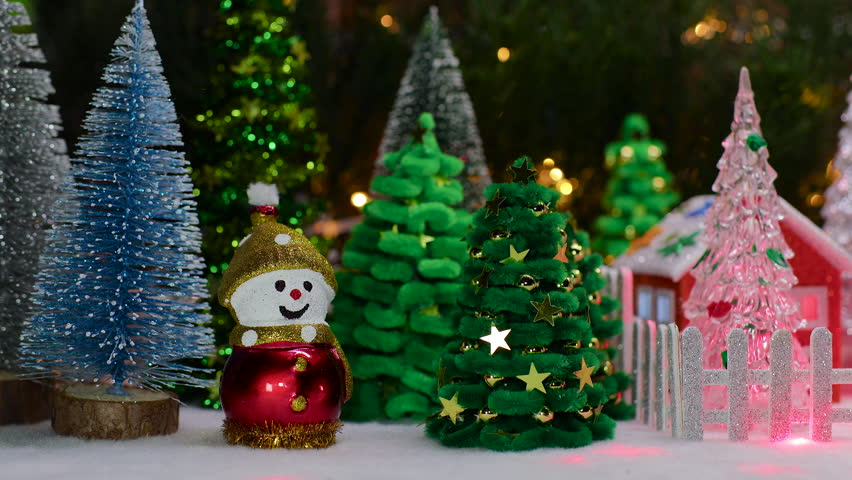 Two houses and a snowman on a sled and Christmas trees behind a fence surrounded by Christmas trees and snowmen with a gnome