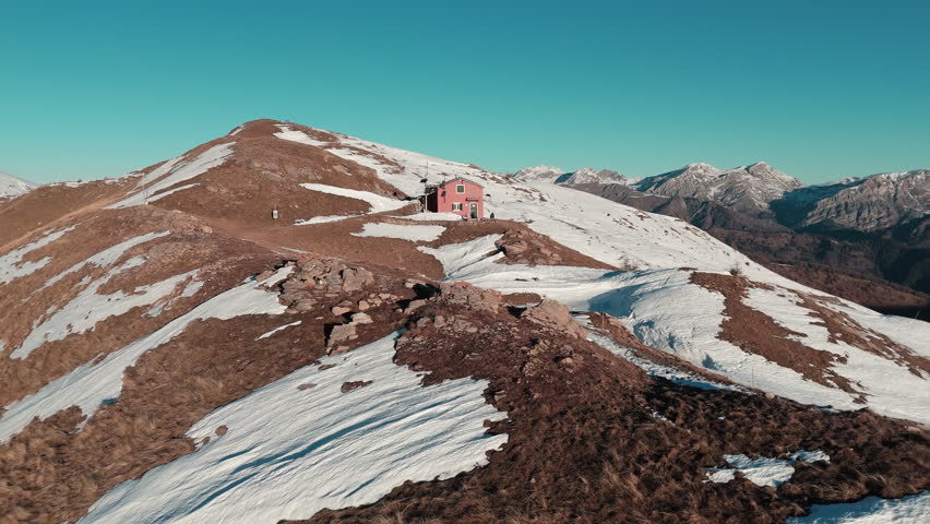 Snowy mountain with distant cabin under a clear sky, peaceful and remote