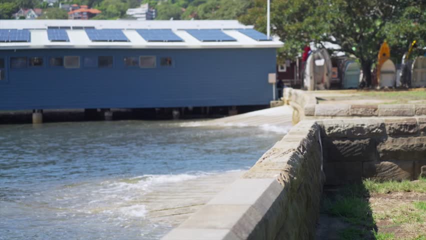 Wide view of a small boat ramp beside a waterfront sailing club building at Double Bay, Sydney, with harbour water moving gently against the concrete edge.