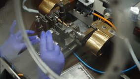 Gloved technician performs precision microelectronics assembly in a cleanroom, operating a wire bonding machine to position and inspect a microchip component under a microscope. - Powered by Shutterstock - Get 15% off with code: PIKWIZARD15