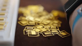 Close-up of gold-plated microchip leadframes scattered on a workbench beside a tray during electronics manufacturing, highlighting precision components and selective focus - Powered by Shutterstock - Get 15% off with code: PIKWIZARD15