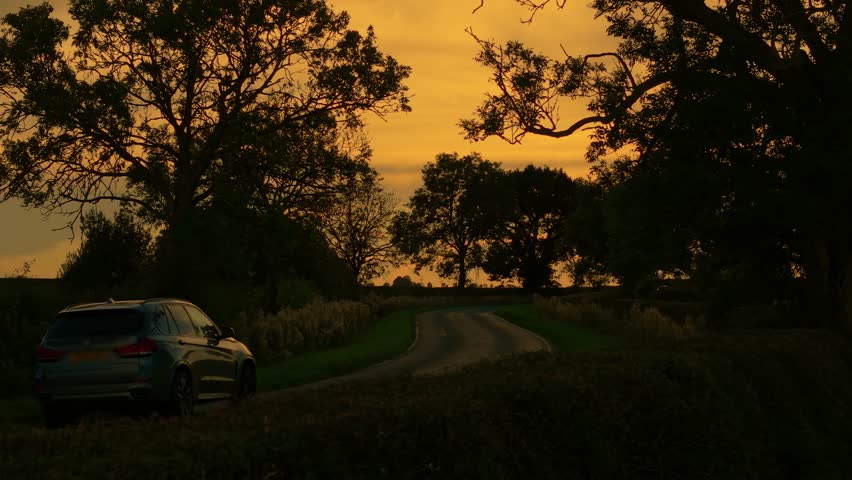 SUV driving on countryside road during sunset. Car traveling highway, exploring countryside, sunset landscape. Automobile moving along rural roadway at sundown