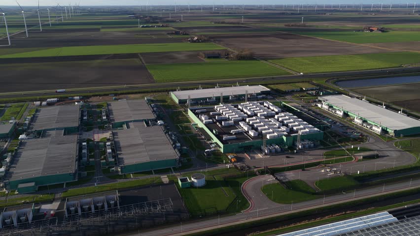 Aerial view of the AI Data Center, a complex of buildings nestled near windmills, amidst fields and highways, creating a contrast in Middenmeer, Netherlands.