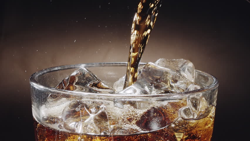 Close-up shot of cola being poured into a glass on the table with visible foam, fizz and rising carbonate bubble.