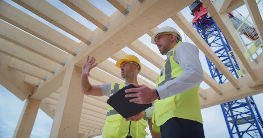 Low Angle View of Two Male Construction Professionals Discussing Commercial Residential Building Design, Using Digital tablet, Planning Real Estate Development Strategy on Business Construction Site.