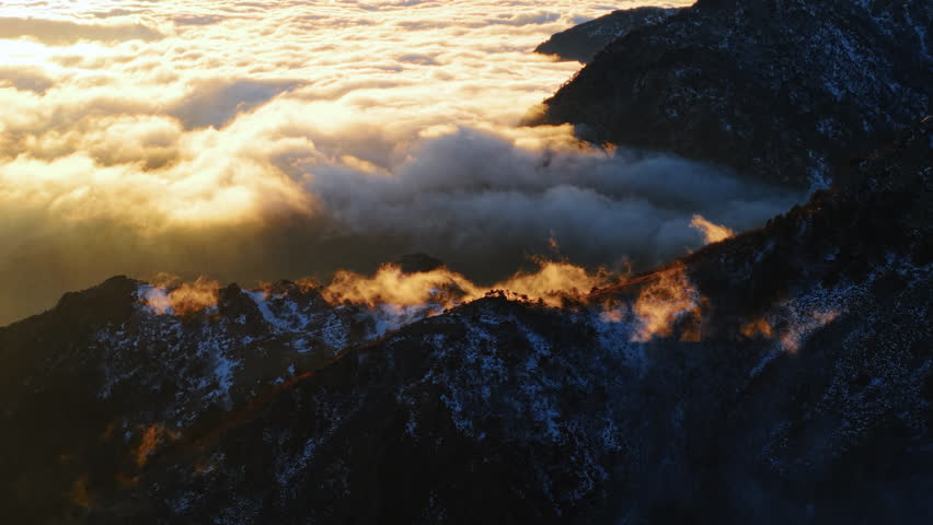Aerial View of Soft Clouds Flowing Over Frozen Mountains