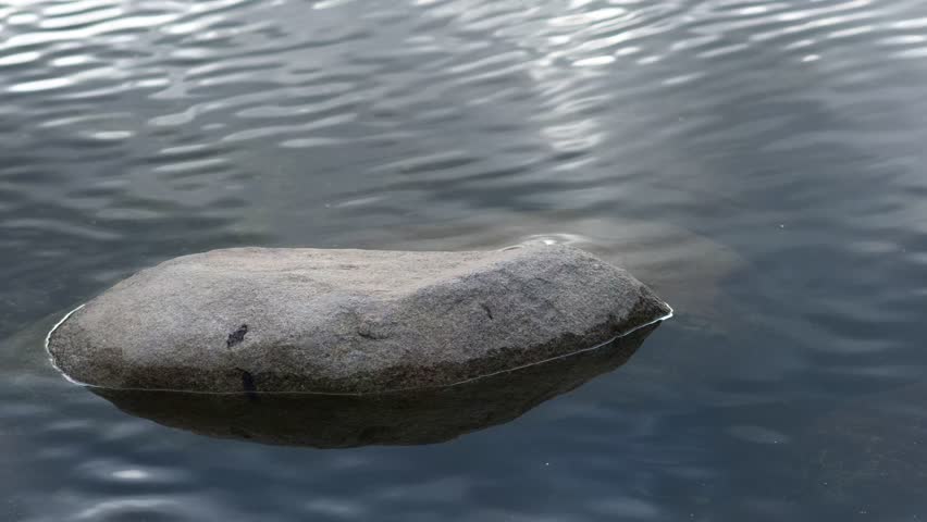 small rock on the still river steam with reflection of blue sky and shade wave from wind blow