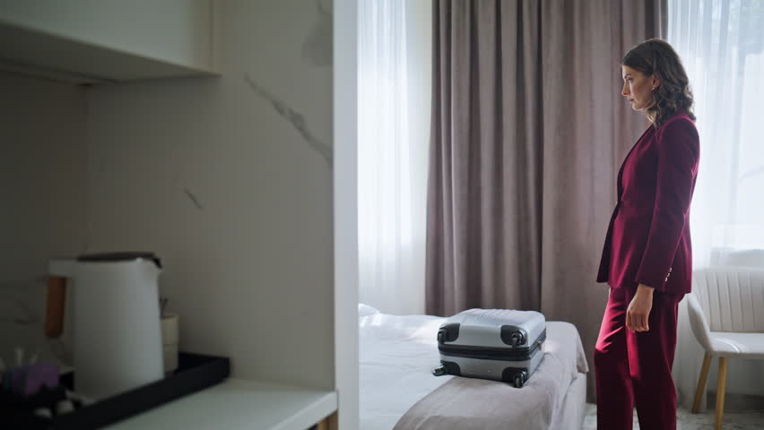 Business lady unpacking luggage on comfortable bed. Elegant suit businesswoman taking out clothes from suitcase in modern light hotel room. Confident woman guest check in luxury motel. Travel concept
