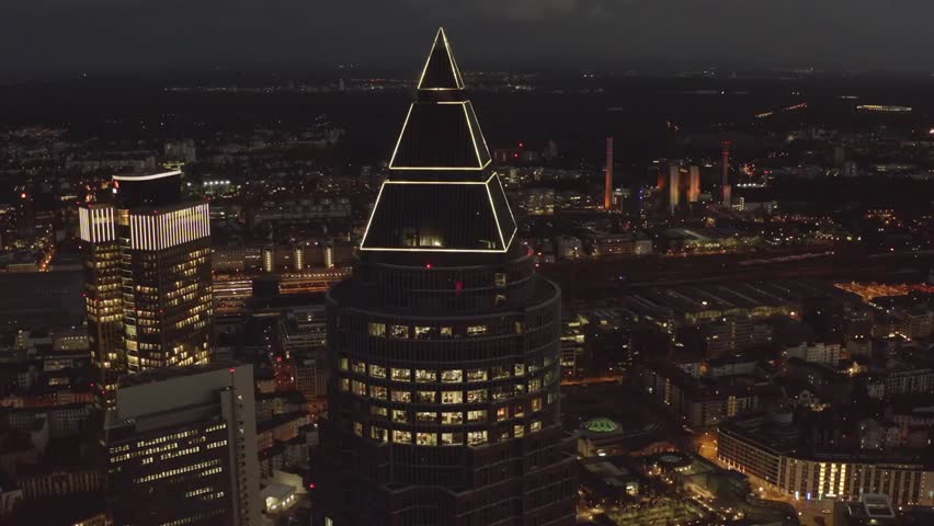 Aerial night view of Messeturm skyscraper in Frankfurt am Main, Germany, with city lights illuminating the modern urban skyline.
