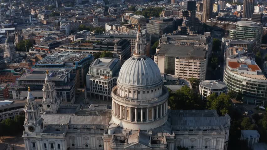 Aerial flyover of Saint Paul’s Cathedral in London, UK, tilting down on its decorated dome and tower with cross under bright afternoon sunlight.