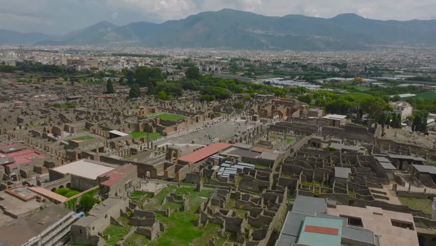 "Aerial view of ancient Pompeii ruins in Italy, showing the volcanic destruction, historic city layout, and modern city with mountains in the background."