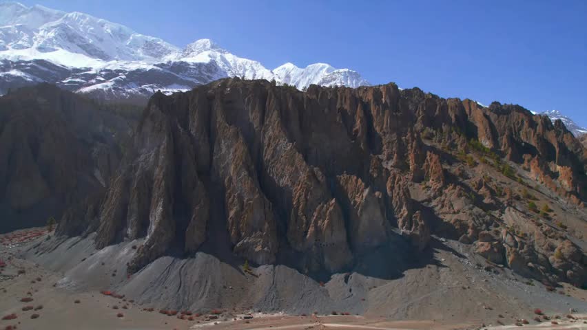 Aerial revealing view of rock formations and snow-capped peaks along the Annapurna Circuit in Nepal, showcasing the majestic Himalayas.