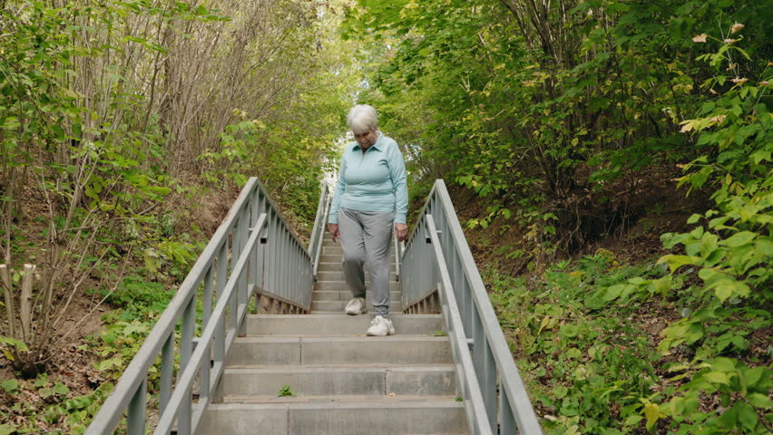 Elderly woman walking down outdoor stairs and feeling sudden knee pain. High quality 4k footage