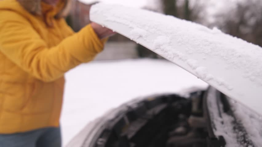 Female Driver Slowly Closes The Snow-Covered Car Engine Hood