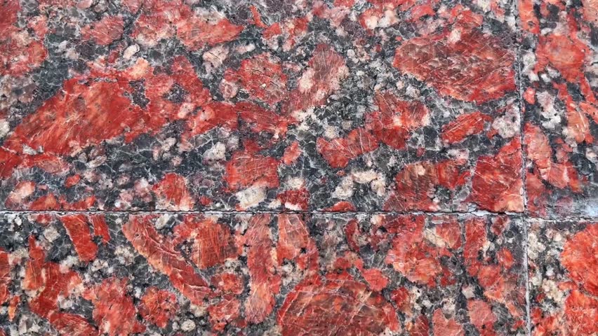 Close-up view of a polished smooth granite wall with natural stone grain and multicolored mineral texture. Architectural stone background suitable for construction, interior design, surfaces, and material concepts