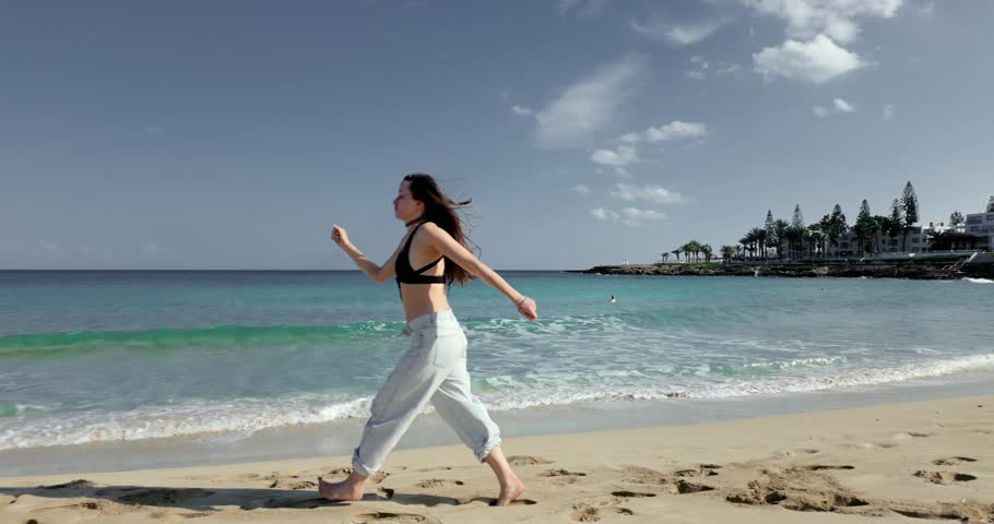 Young Woman Running Along Sandy Beach, Pausing to Watch the Sea and Walking Back in Slow Motion at Fig Tree Bay Cyprus