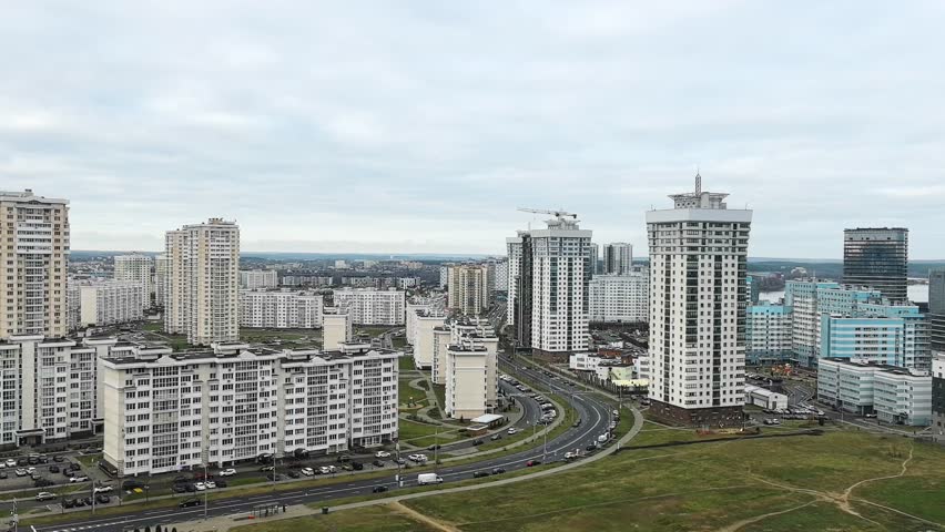 The view captures a skyline filled with tall buildings and busy streets. People move around the city in different directions. The weather is clear with clouds in the sky.