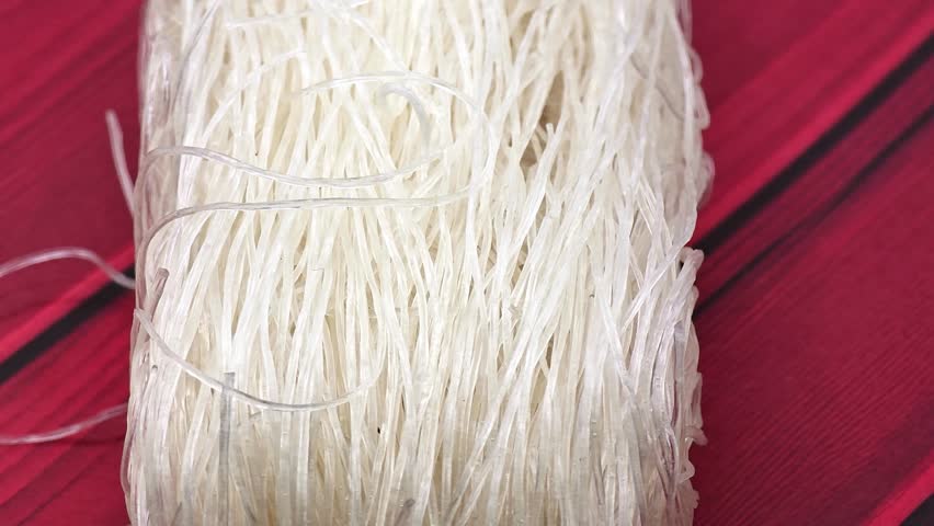Dry rice vermicelli noodles on vibrant red wooden background texture