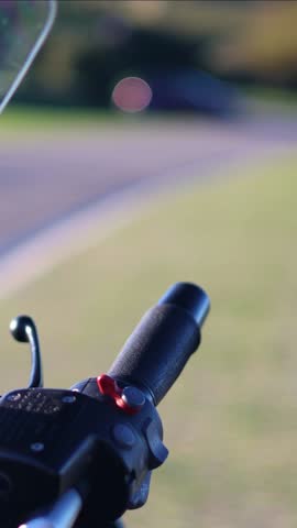 vertical Close-up shot of an elderly man wearing black leather gloves starting his motorcycle, pressing the red engine start button on the handlebar before heading out for a ride on a sunny day