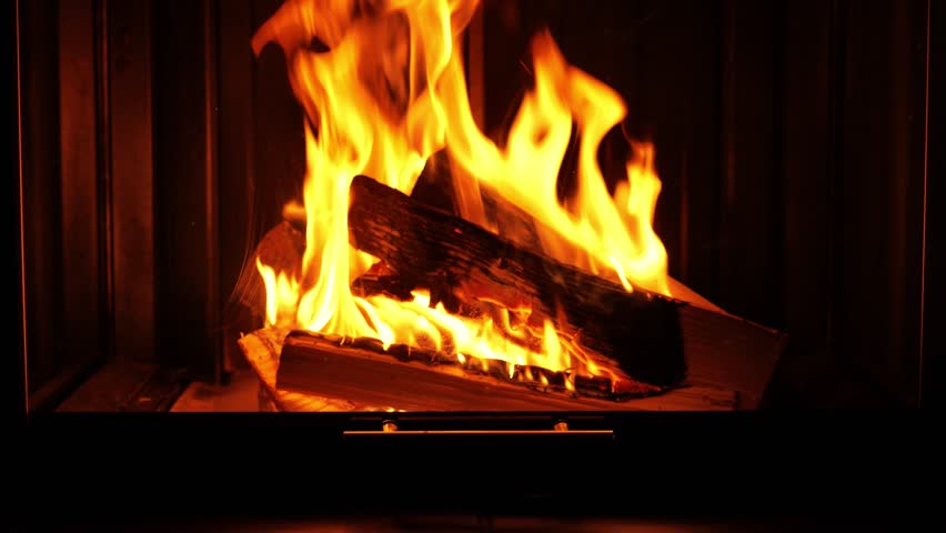 A glass fireplace in a dark room. Flames, smoke, and sparks behind the glass. A cozy fireplace with live fire. 4k footage