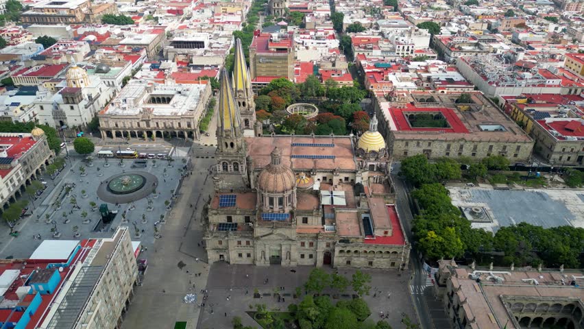 High aerial drone shot captures the iconic Guadalajara Cathedral, main plaza, and historic downtown architecture on a bright day in Jalisco, Mexico.
