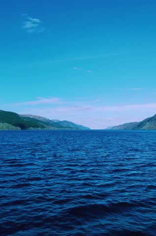 Serene lake scene with rippling water and lush green mountains under a clear blue sky