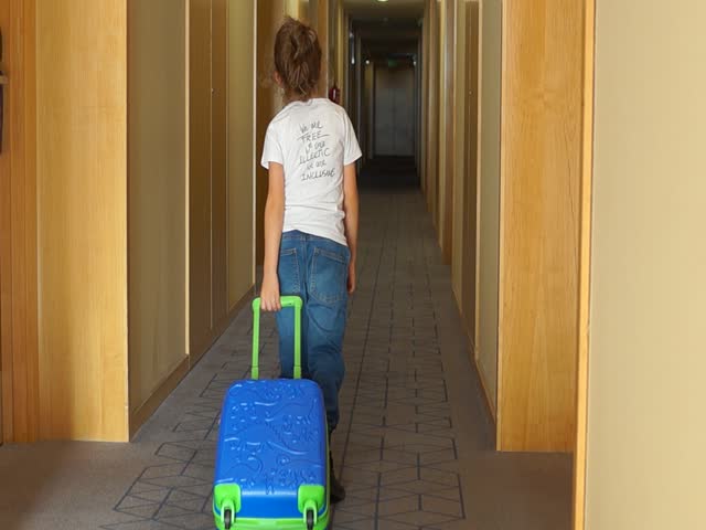 Young Girl Pulling Blue Luggage in Bright Hotel Corridor