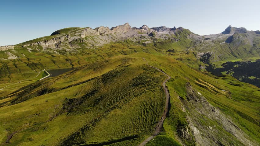 Aerial footage of a male hiker walking along an alpine ridge near Engstlensee on the Via Alpina in Switzerland. Scenic mountain landscape, hiking trail, solitude and outdoor adventure.