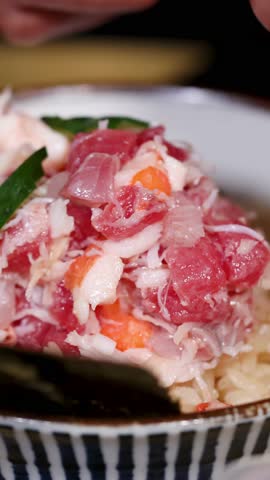 Close-up shot of a chef placing cucumber slices on a fresh kani don seafood bowl