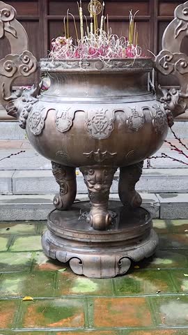 A detailed vertical shot of a large bronze incense burner filled with smoldering sticks.