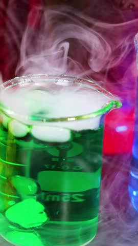 A vibrant green liquid in a glass beaker reacts with dry ice, creating thick smoke.