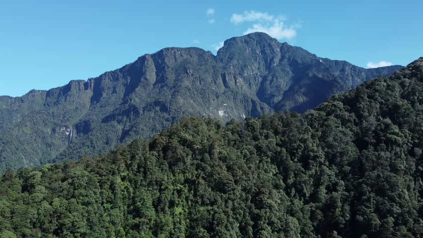 Forest covered mountain cliffs with blue sky background, capturing the untouched beauty of Indonesian tropical highlands.