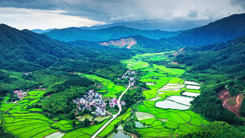 Aerial shot of beautiful rural village with green paddy fields and mountain landscape in southern China