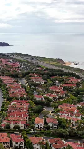 Aerial view of coastline with highway running between ocean waves and luxury cliffside homes under cloudy sky showing scenic coastal landscape