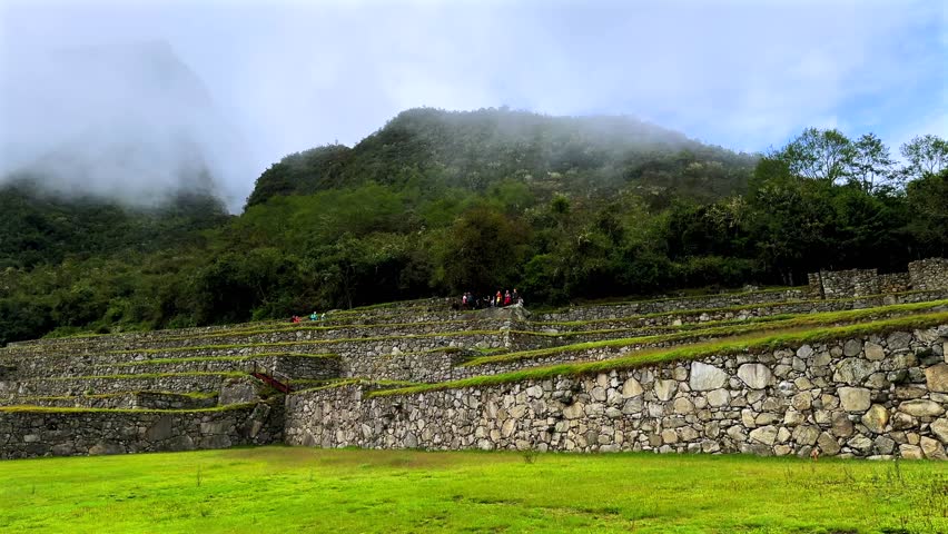 Morning foggy sunrise Inca trail Machu Picchu stonework tourist circuit landscape sunny fog clouds Peruvian Andes Peru Perú historic Inca Sanctuary Temple rainy season lush green jungle pan left