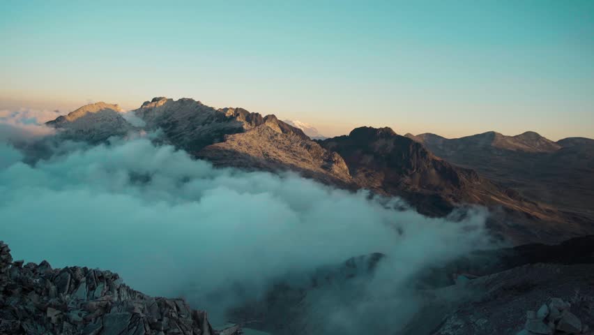 A cinematic aerial time-lapse of thick clouds moving across the rugged Andean peaks of the Cordillera Real. The dynamic atmosphere of the high-altitude Bolivian mountains.