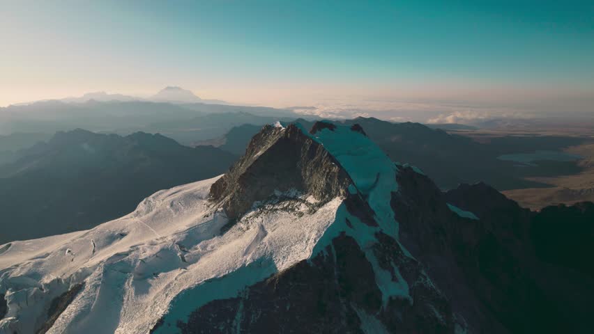 Cinematic orbiting drone shot of a sharp Andean ridge. The snow-capped summits and rugged vertical terrain of the Cordillera Real in high-altitude Bolivia.