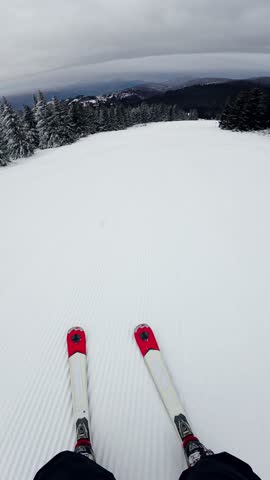 Travel and winter adventure concept. Beautiful POV ski landscape on the mountains. Skier skis down a snowy mountain trail in cloudy weather. Vertical shot